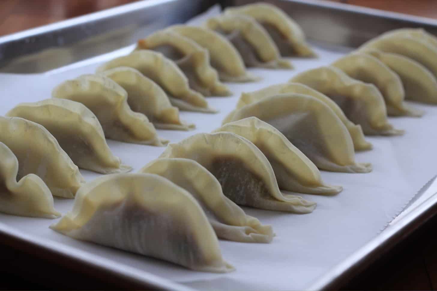 rows of pork gyoza on a parchment lined sheet pan