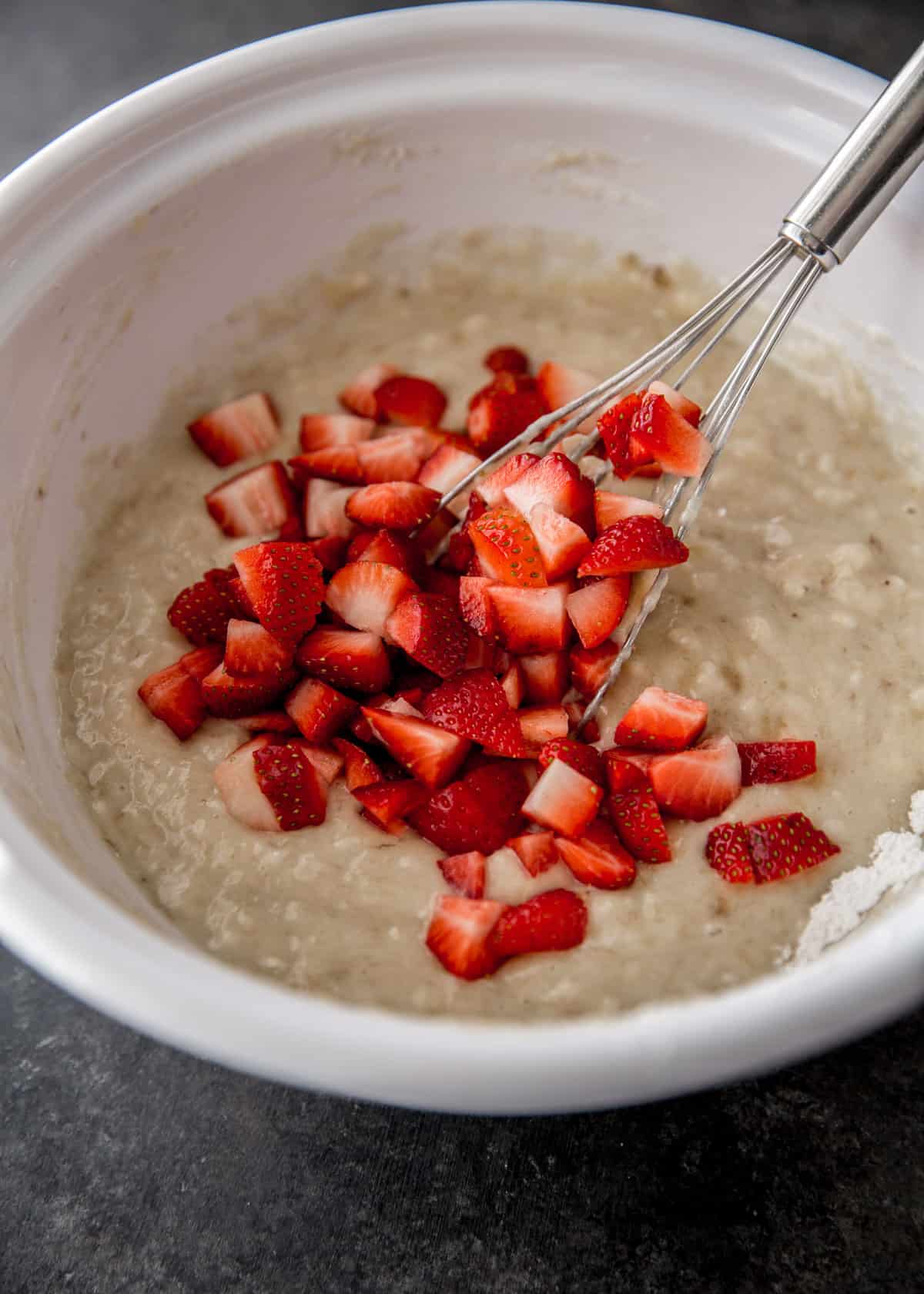 overhead image of mixing cut strawberries into muffin mixture in a white bowl