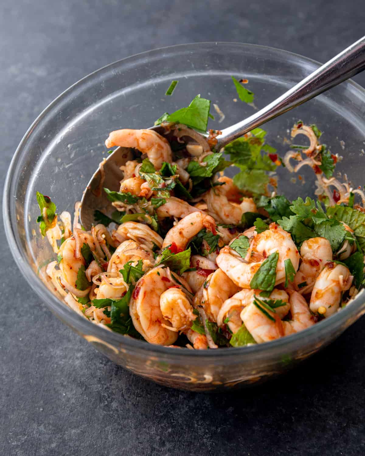 stirring shrimp and herbs in a clear glass bowl