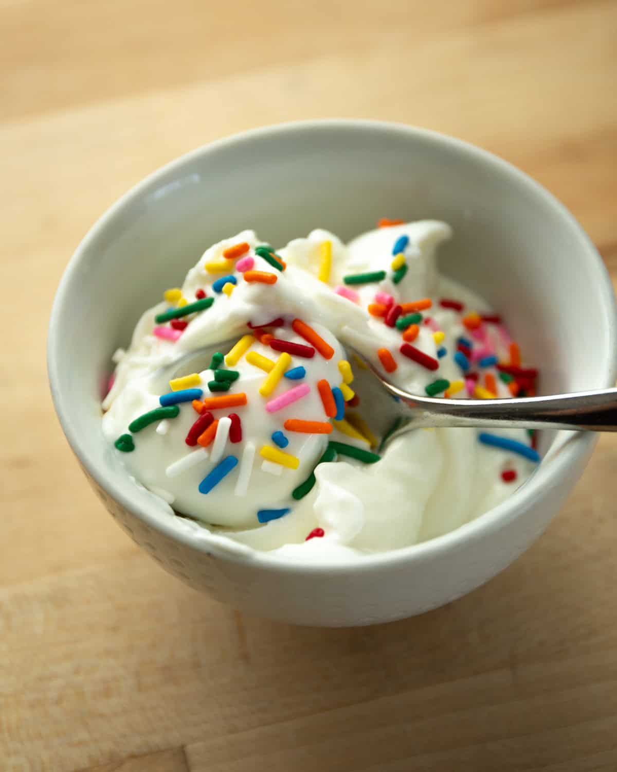 frozen greek yogurt covered in multi-colored sprinkles in a white bowl with a spoon