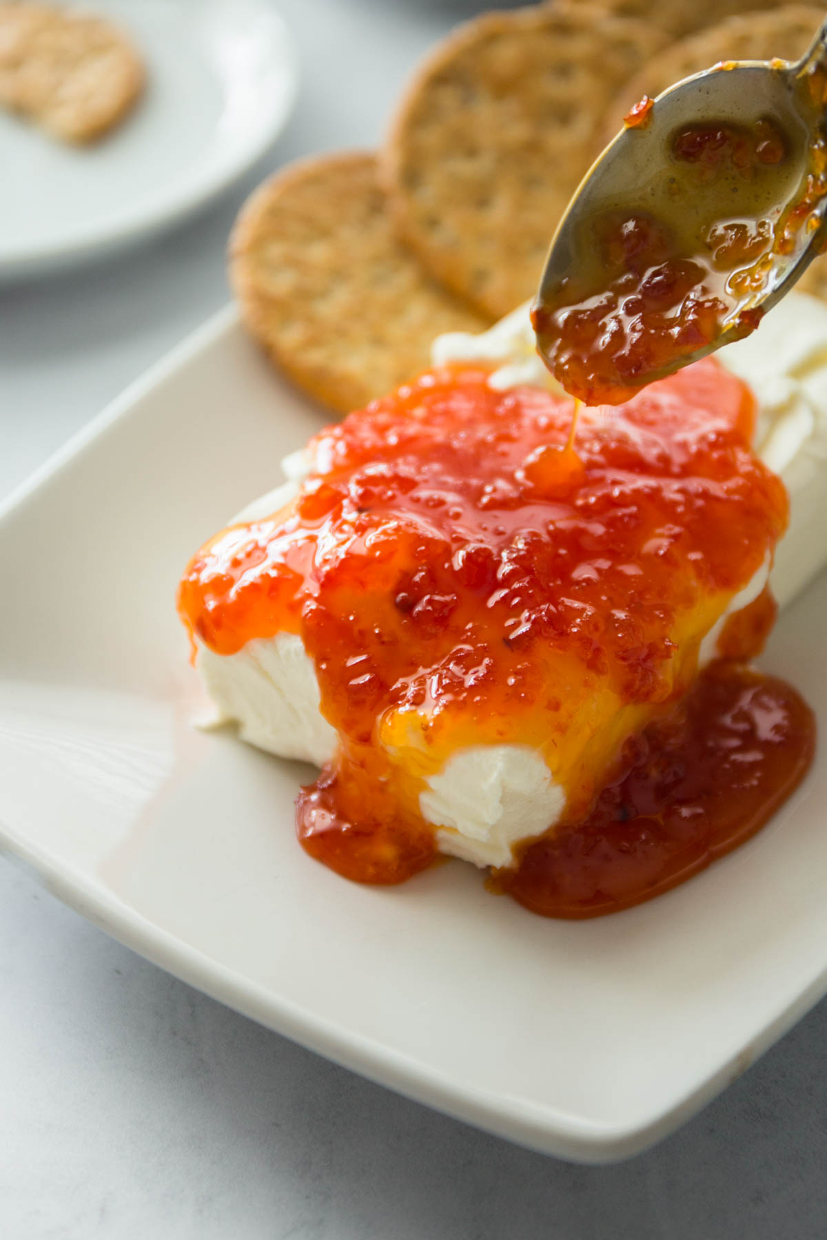 spooning red pepper jelly over cream cheese