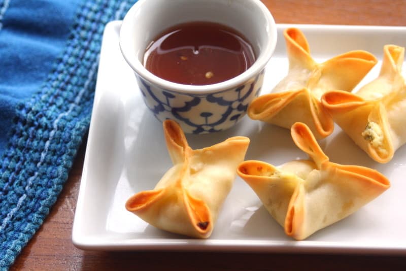 overhead image of crab rangoons on a white tray with a small bowl of chili sauce