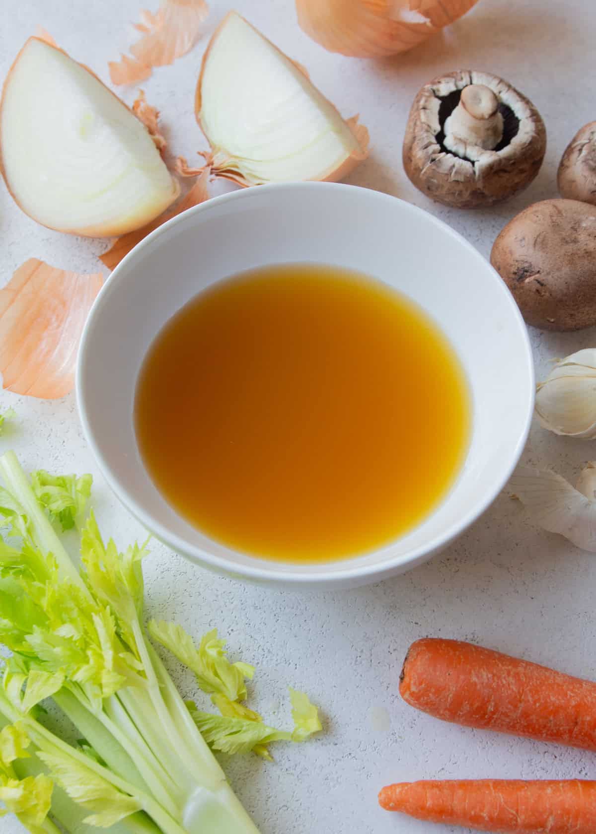 overhead image of vegetable broth in a small white bowl, surrounded by raw vegetables