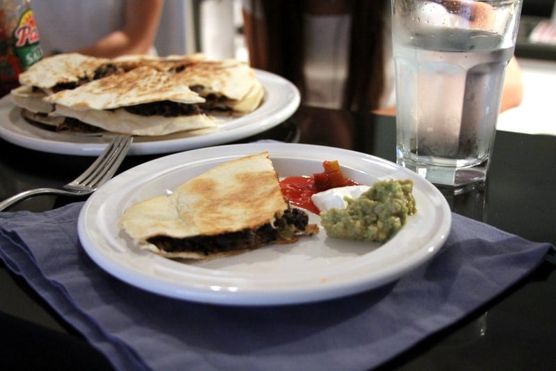 a black bean quesadilla on a white plate with guacamole and salsa