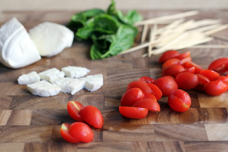 cherry tomatoes, mozzarella, basil and skewers in piles on a wooden cutting board