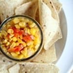 overhead image of corn salsa in a clear glass bowl on a white plate with tortilla chips