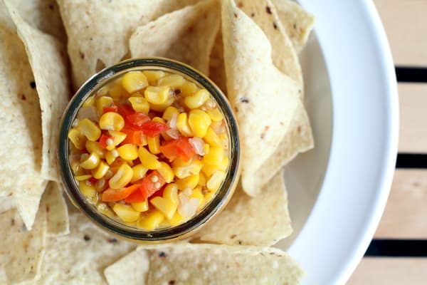 overhead image of corn salsa in a small glass bowl with tortilla chips on a white plate