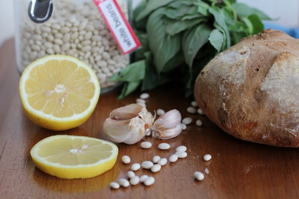 ingredients for white bean bruschetta on a table - lemon, garlic, white beans, basil, bread