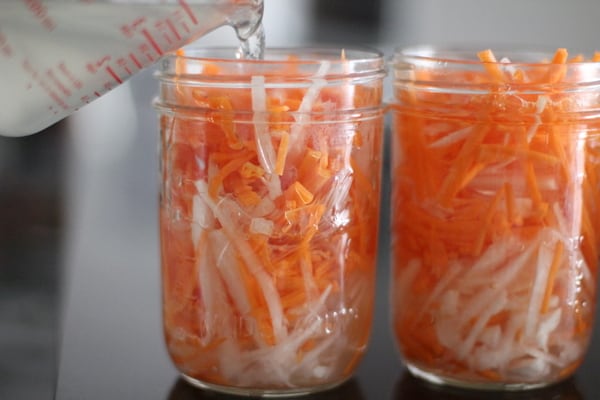 pouring vinegar mixture over carrots and onions in glass jars