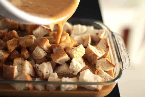 pouring pumpkin mix over bread cubes in a baking dish