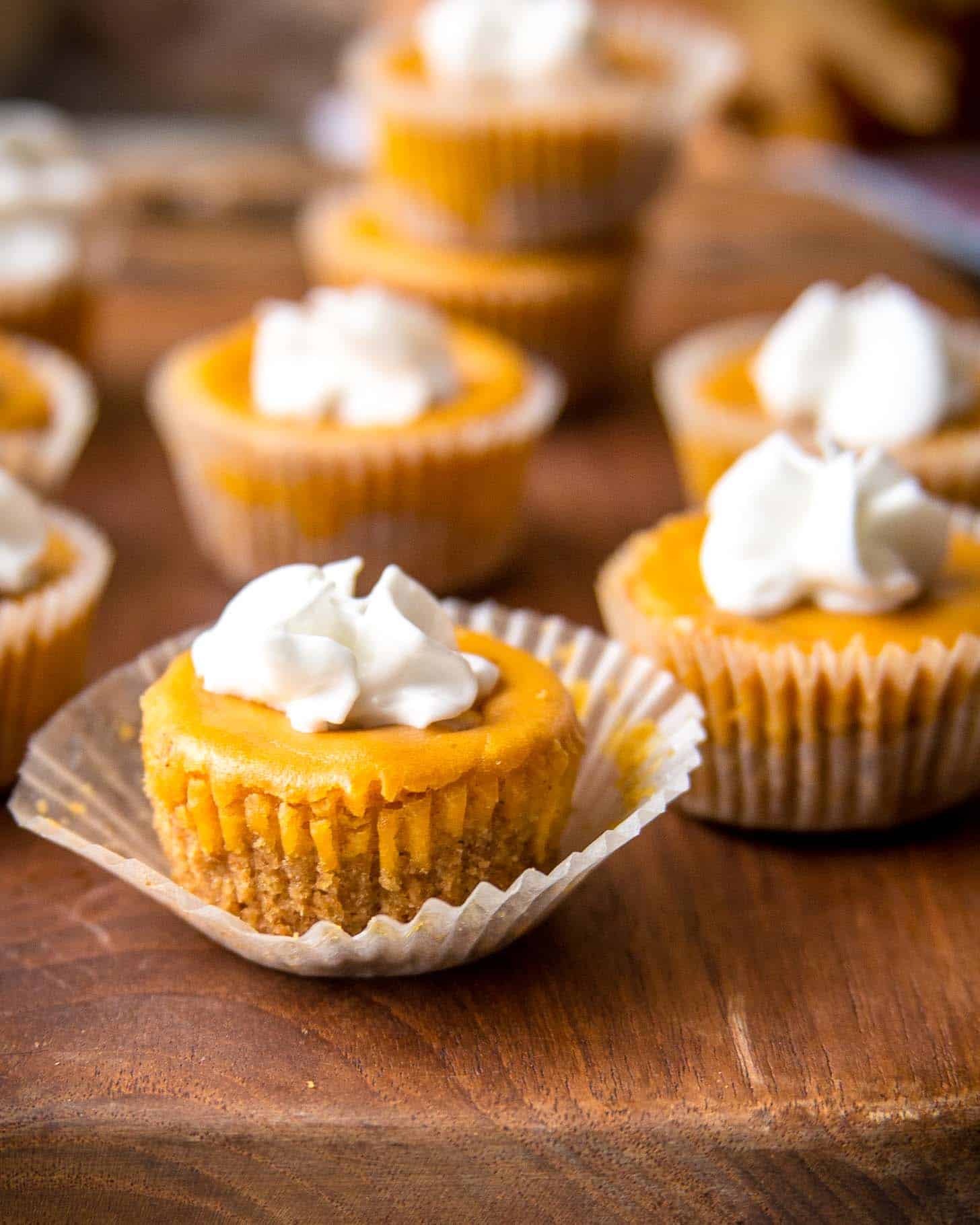 Pumpkin Cheesecake Bites topped with whipped cream on a wood cutting board