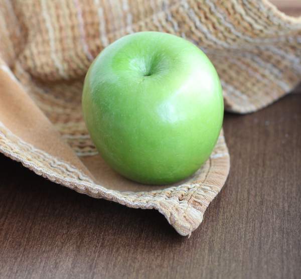 a green apple on a wooden table with a tan towel