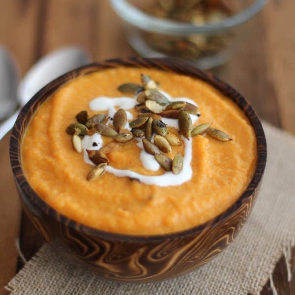 carrot soup in a wooden bowl topped with toasted pepitas