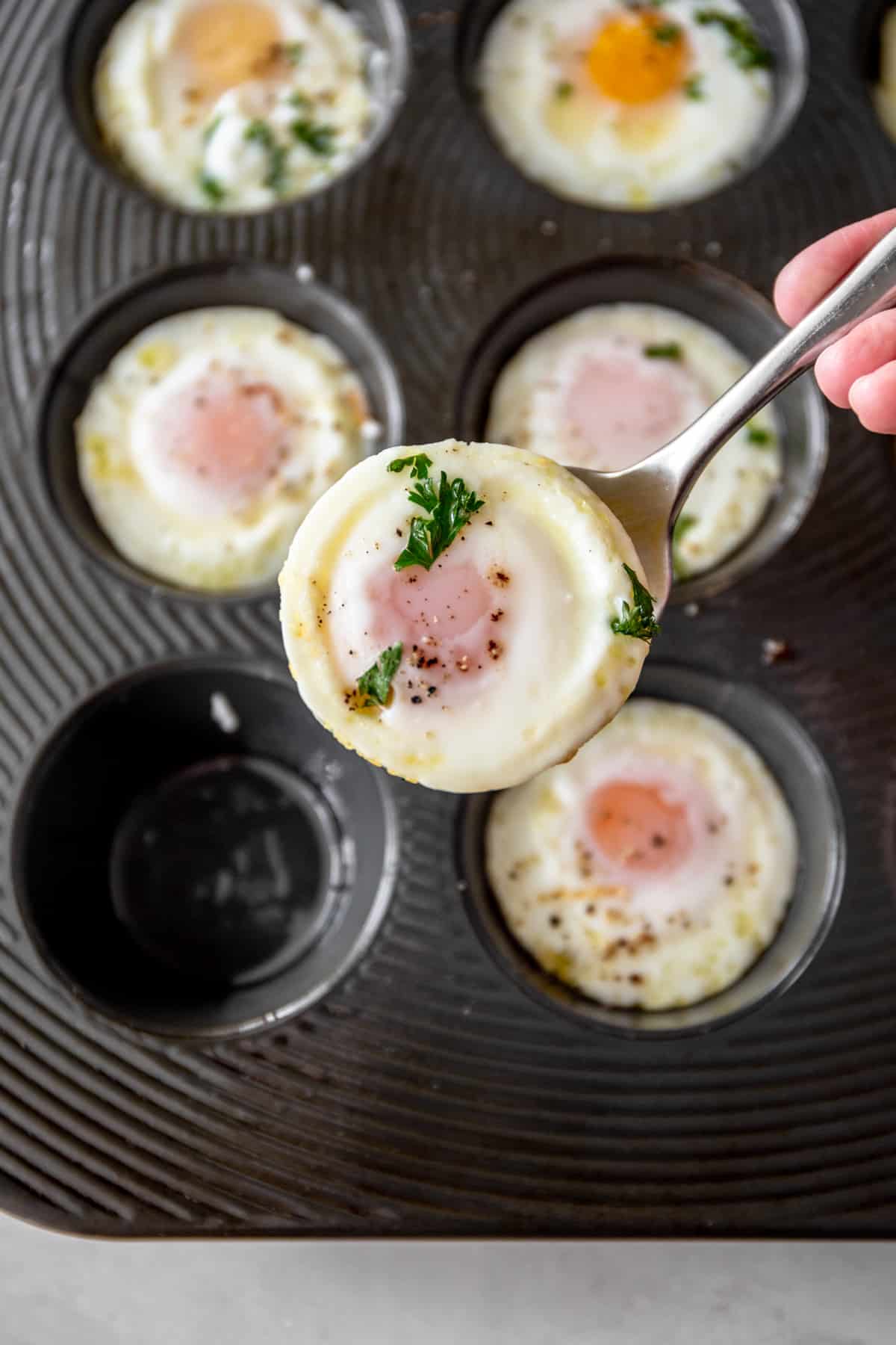 overhead image of a baked egg being removed from a muffin pan