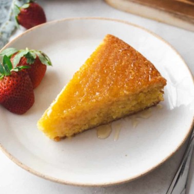 a slice of polenta cake on a white plate with strawberries