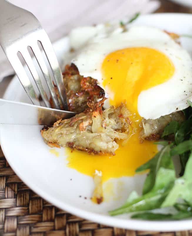 cutting a fried egg and hash browns on a white plate