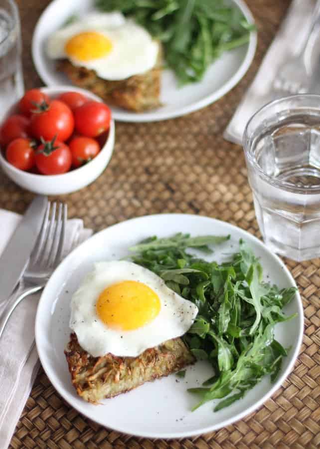 overhead image of hash browns with a fried egg and arugula on a white plate