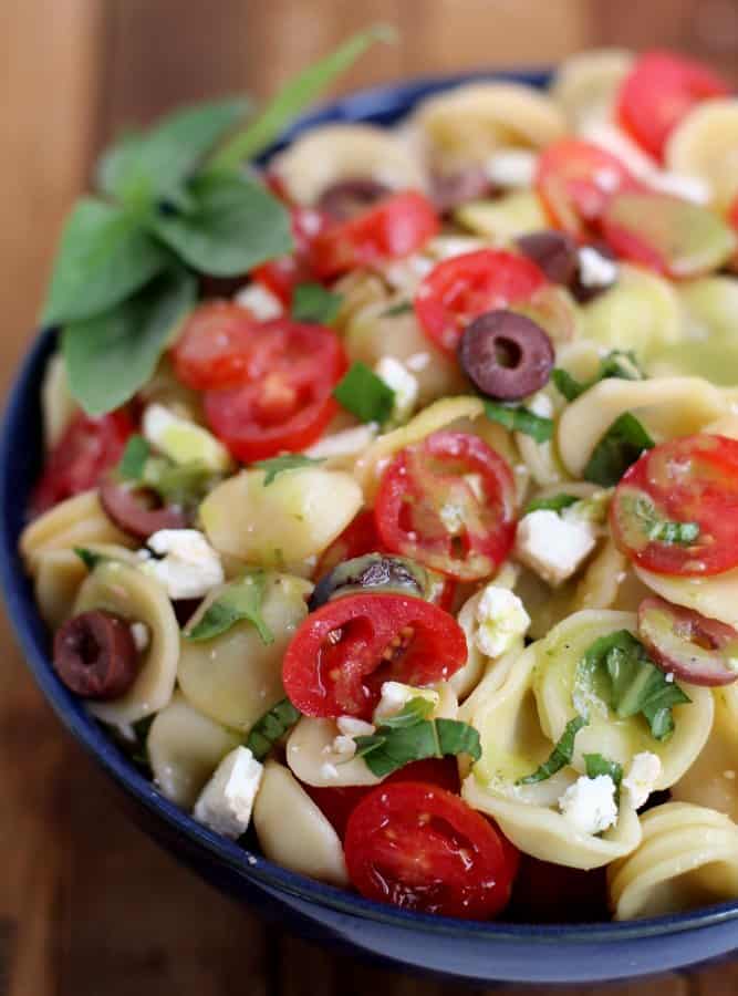 greek salad in a navy blue bowl and topped with basil