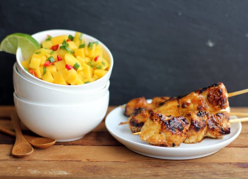 chicken on a white plate and mango salsa in a small white bowl