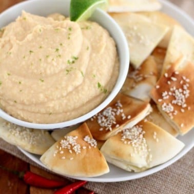 white bean dip in a white bowl with sesame pita chips on a white plate