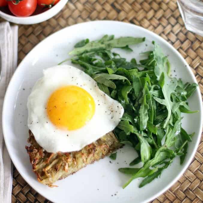 overhead image of hash browns with a fried egg and arugula on a white plate