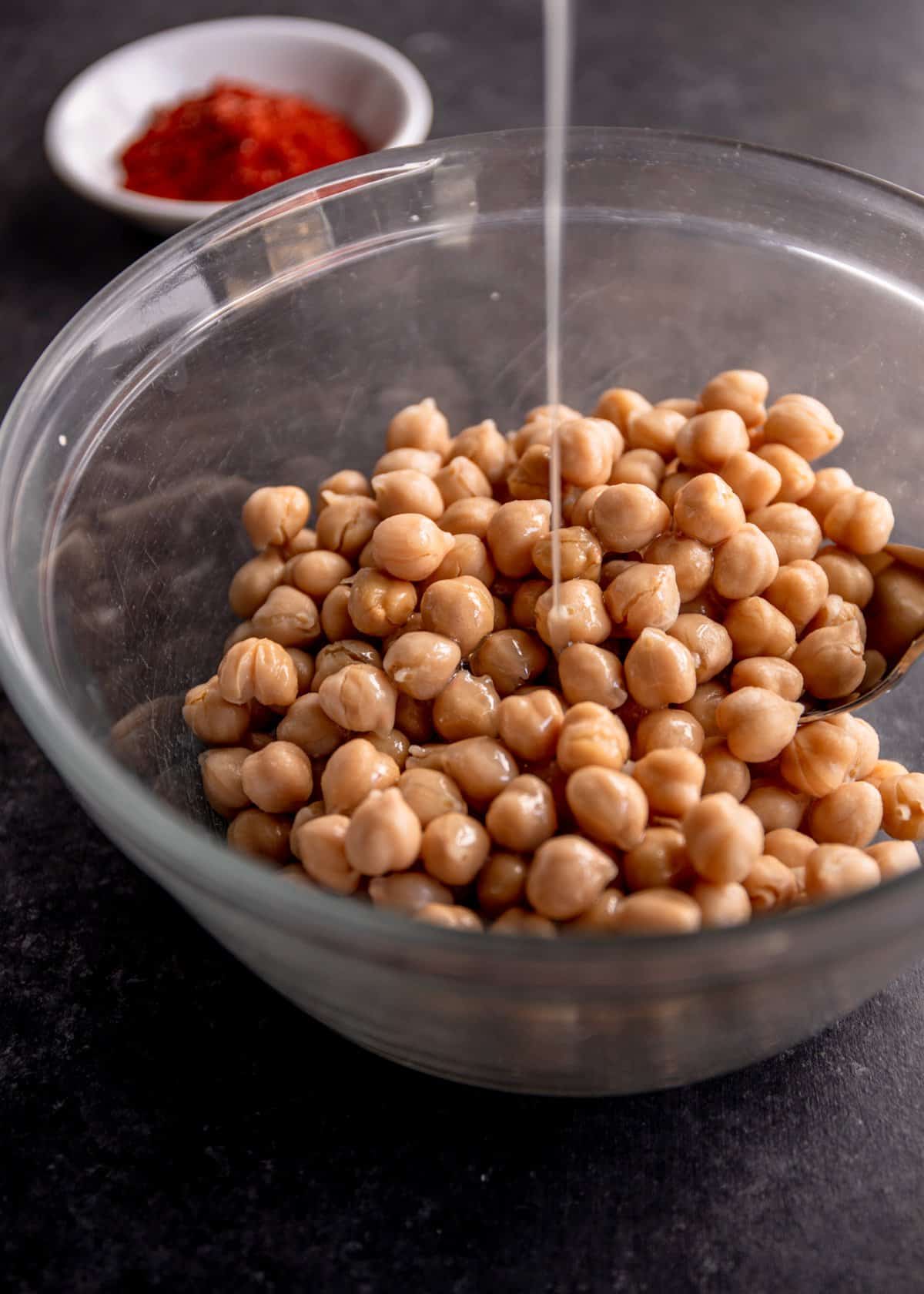 drizzling oil over chickpeas in a glass bowl