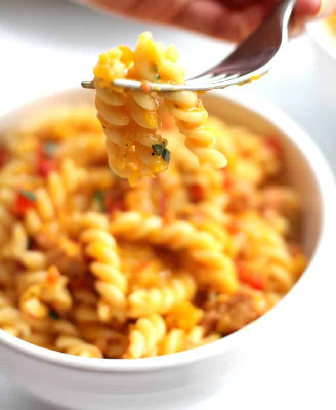 a forkful of cheesy pasta over a white bowl full of pasta