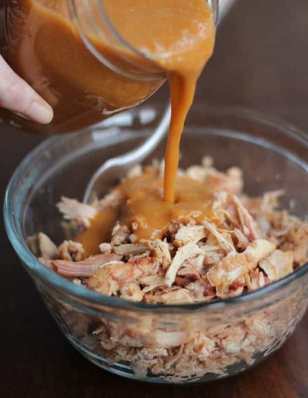 pouring sriracha sauce over pulled chicken in a clear glass bowl