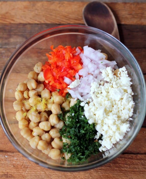 chickpeas, red peppers, onions, herbs and cheese in a clear bowl