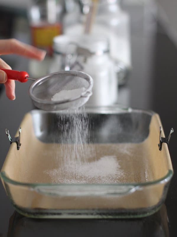 sprinkling powdered sugar over a parchment lined baking dish