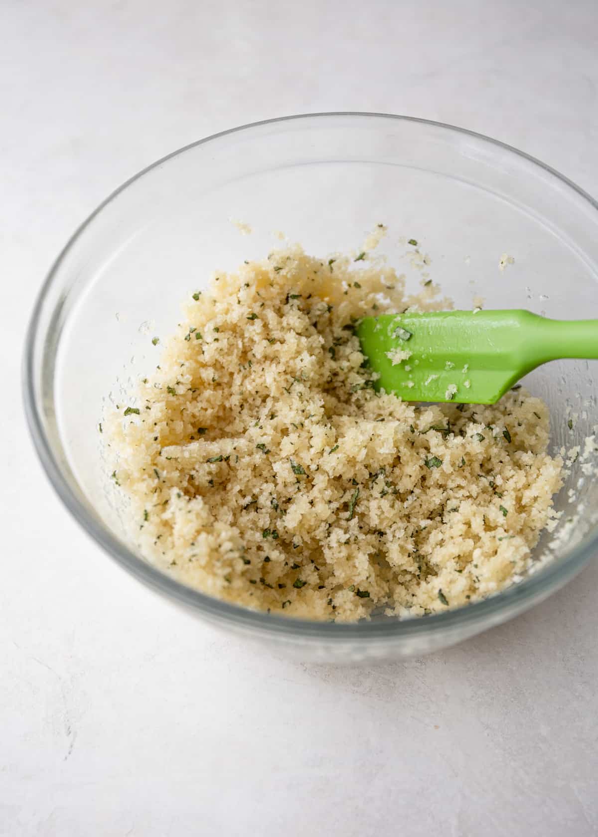 mixing breadcrumb topping for pasta bake in a clear glass bowl