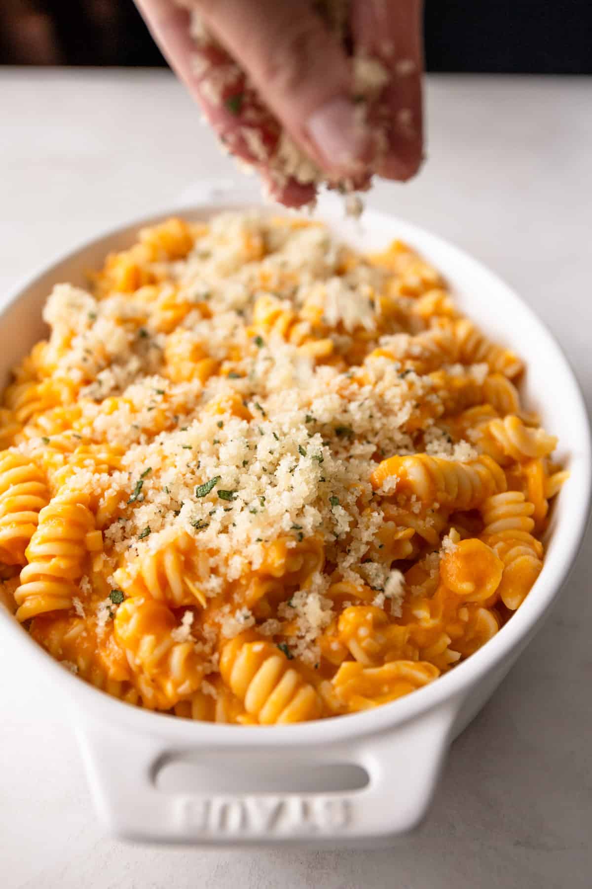 adding panko topping to a dish of sweet potato mac and cheese