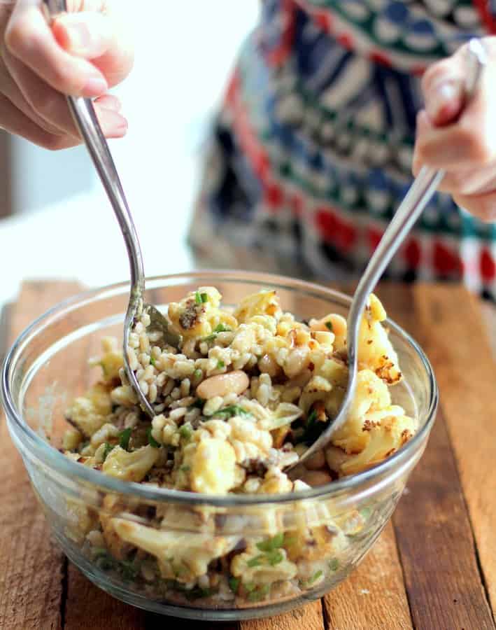 mixing cauliflower salad in a clear glass bowl