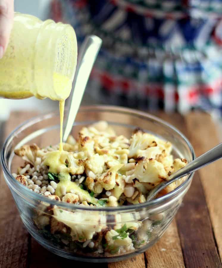 adding dressing to warm cauliflower salad in a clear glass bowl