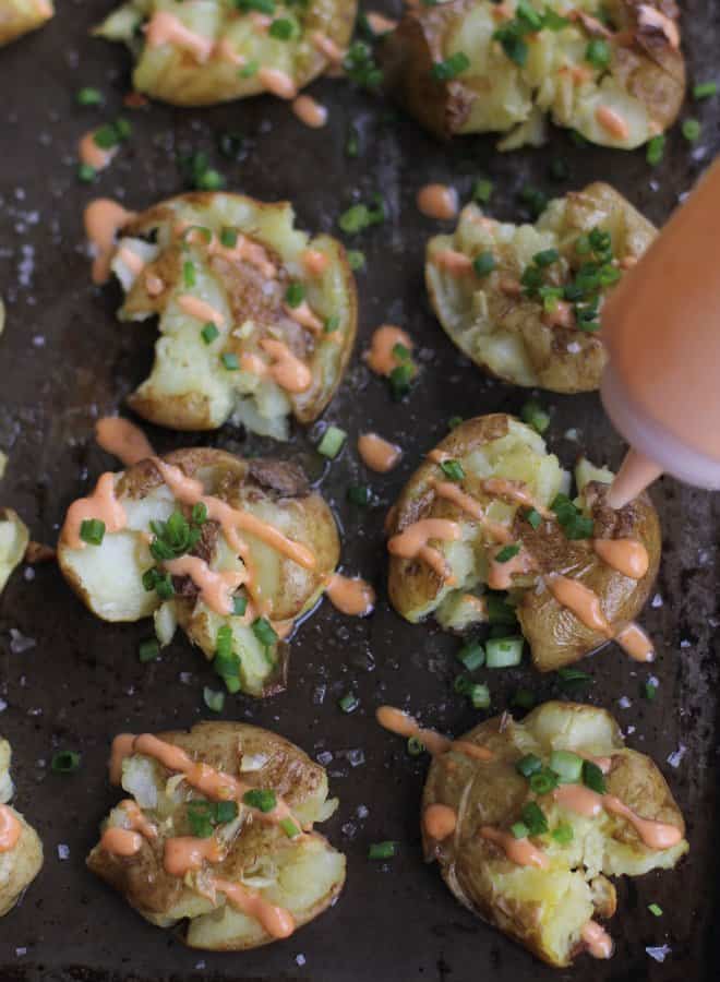 adding sriracha to smashed potatoes on a sheet pan