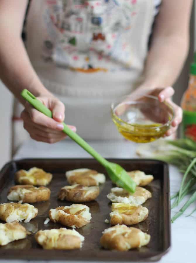 brushing oil on smashed Potatoes on a sheet pan