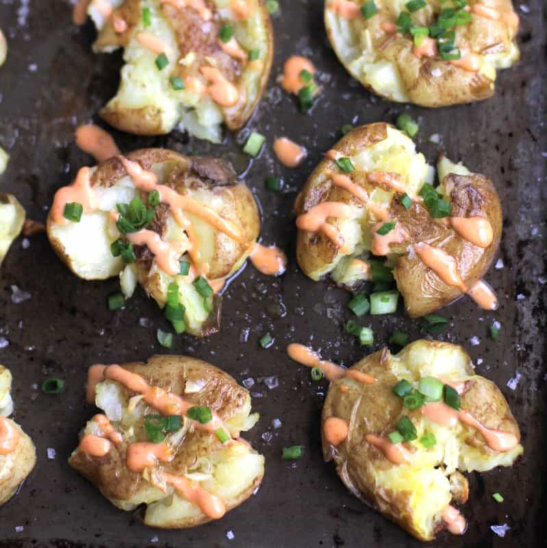smashed potatoes topped with sriracha and chives on a sheet pan