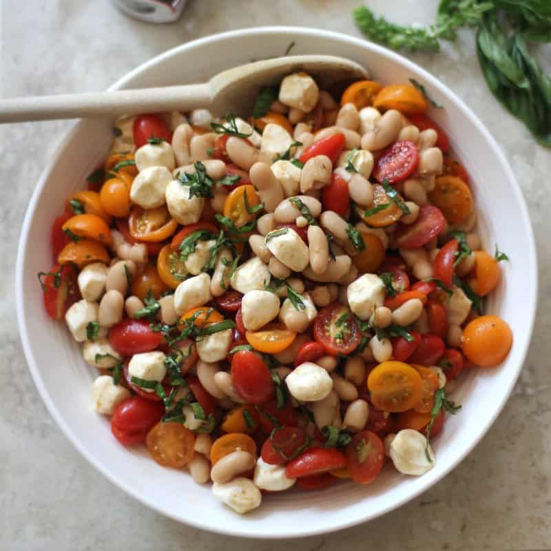 caprese Salad in a white bowl with a wooden spoon