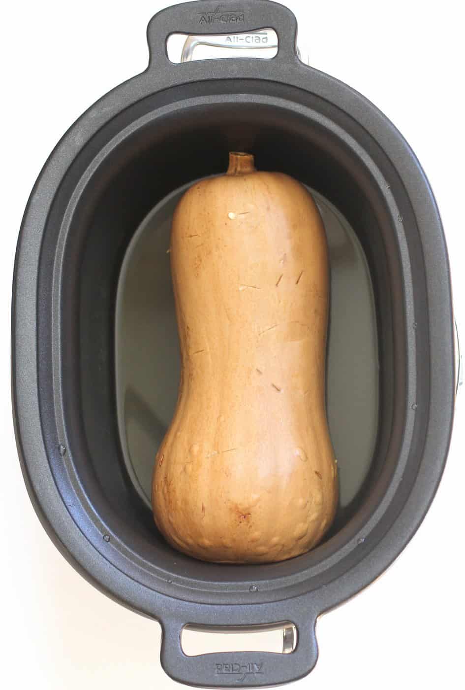 a raw butternut squash in the bowl of a slow cooker