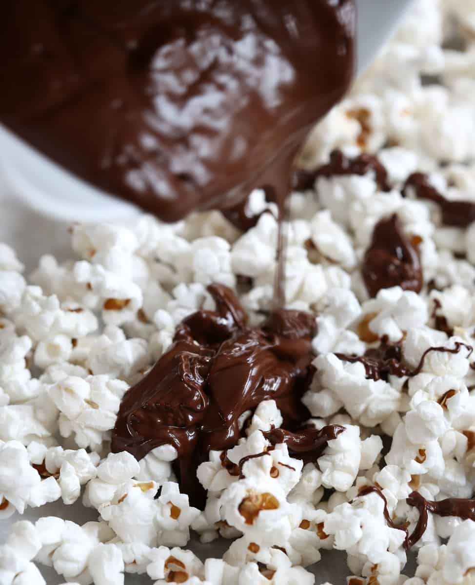 pouring chocolate over popcorn on a sheet pan