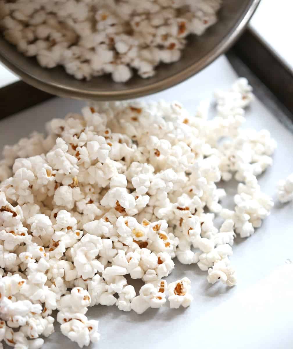 pouring popcorn onto a parchment lined sheet pan