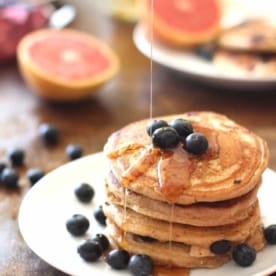 pouring syrup over blueberry pancakes