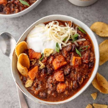 overhead image of a bowl of chili with cheese, sour cream, and green onions on top
