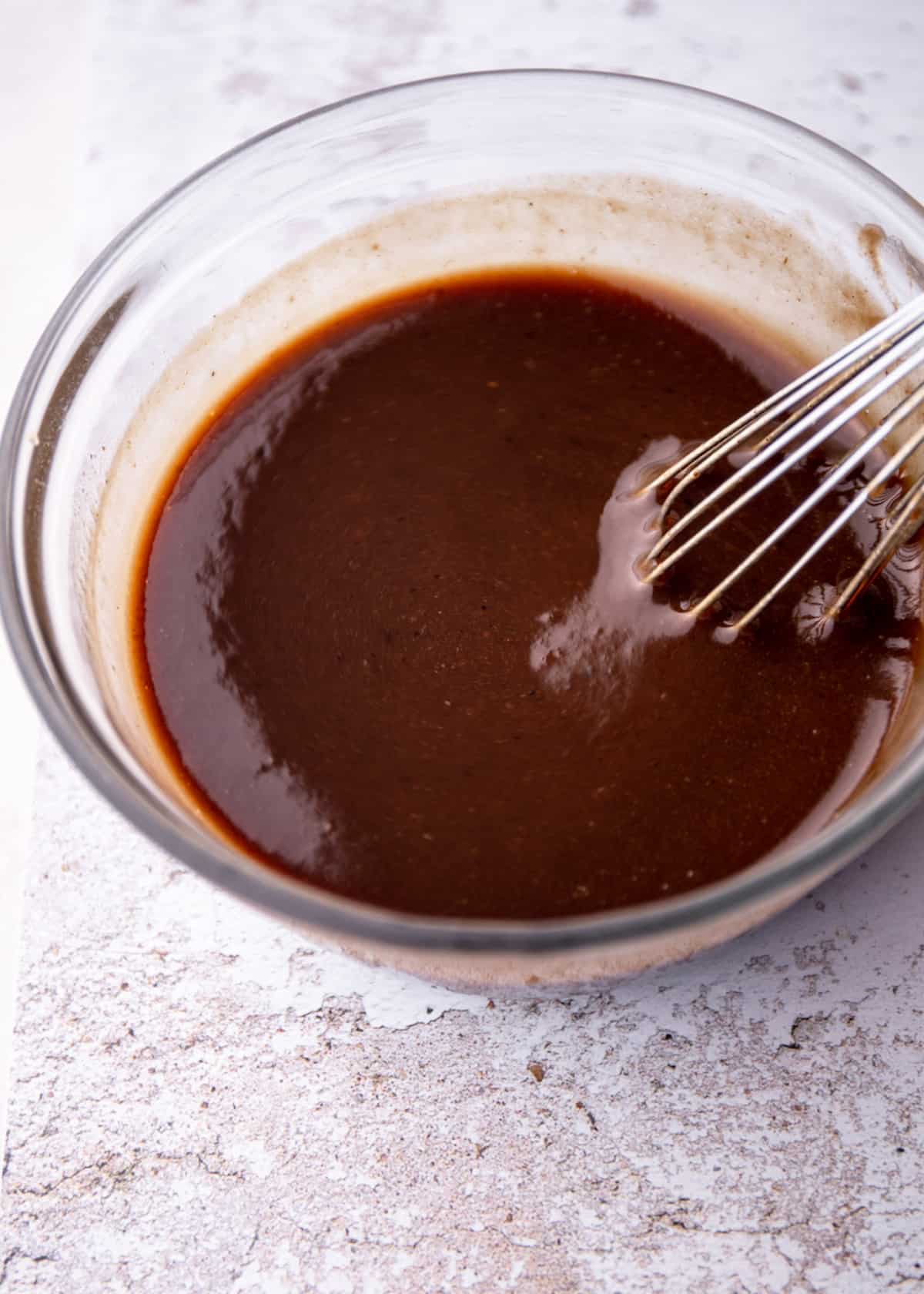 a glass bowl with a whisk and a dark red tamarind-based pad thai sauce