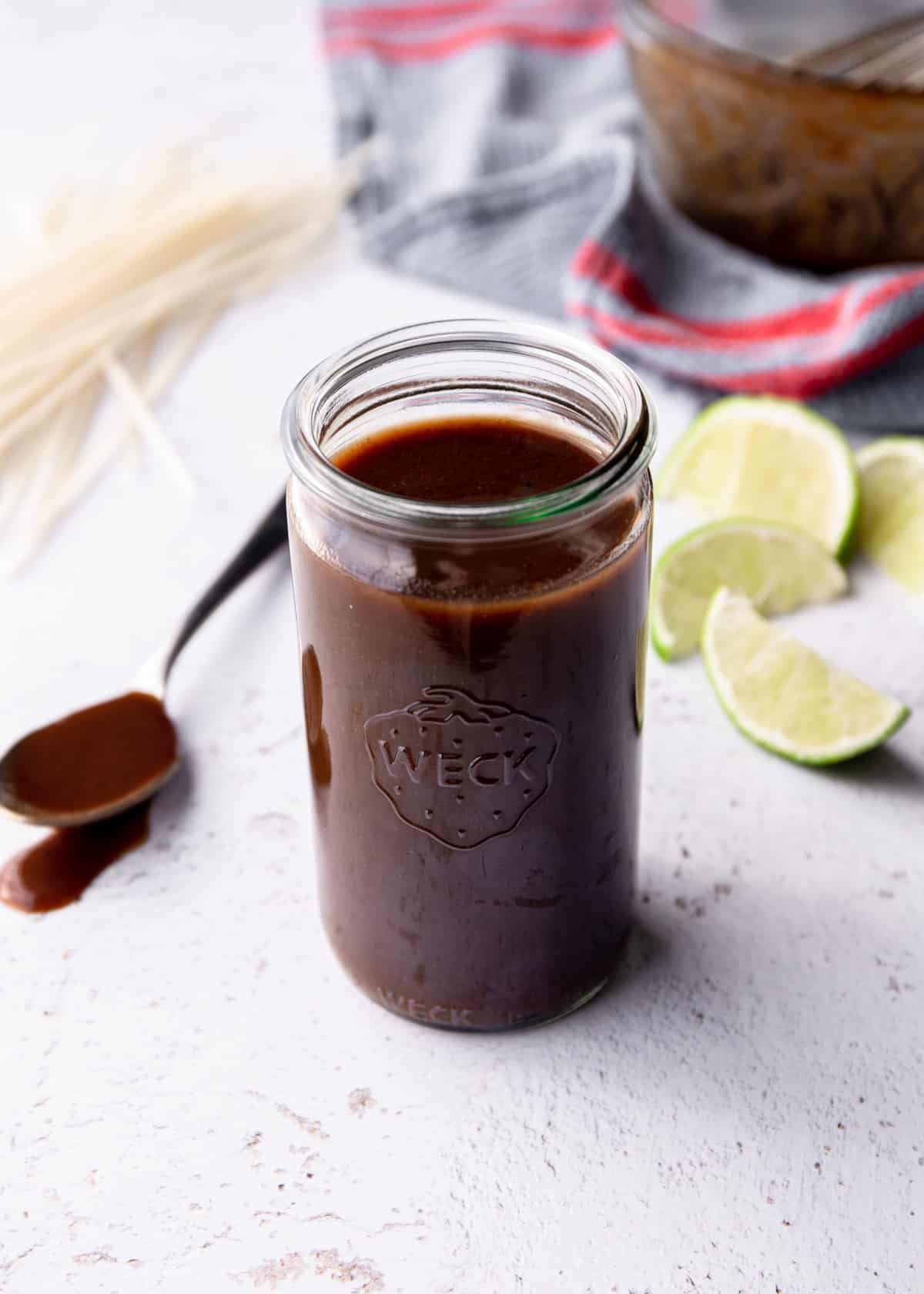 glass jar full of pad thai sauce with lime wedges and rice noodles in the background