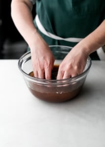 a Caucasian person with hands in a glass bowl full of soaked tamarind paste