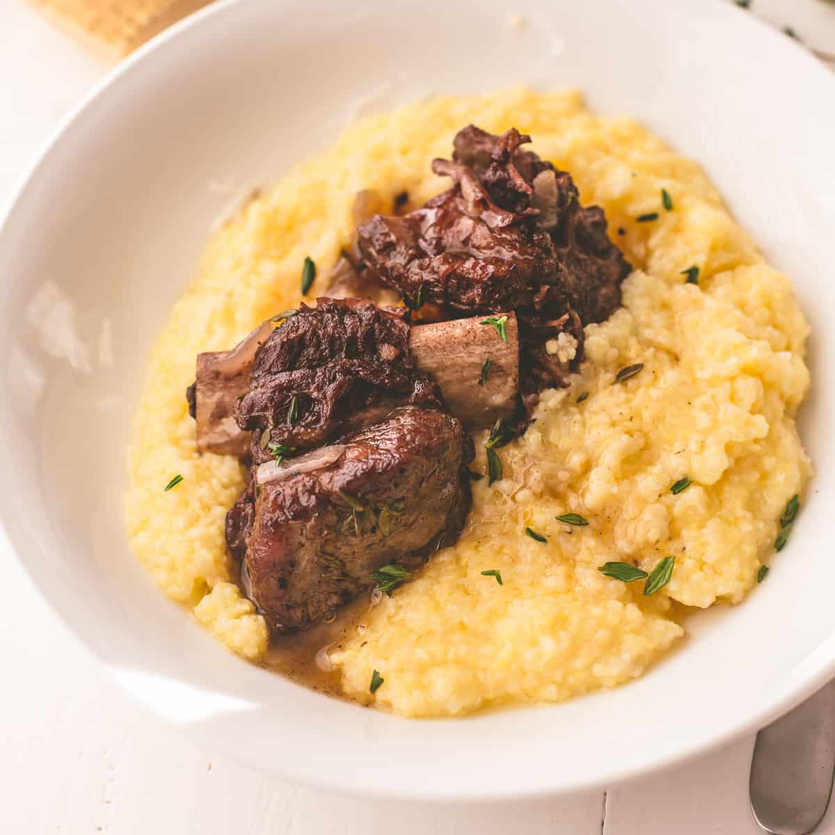 cooked short ribs over polenta in a white bowl