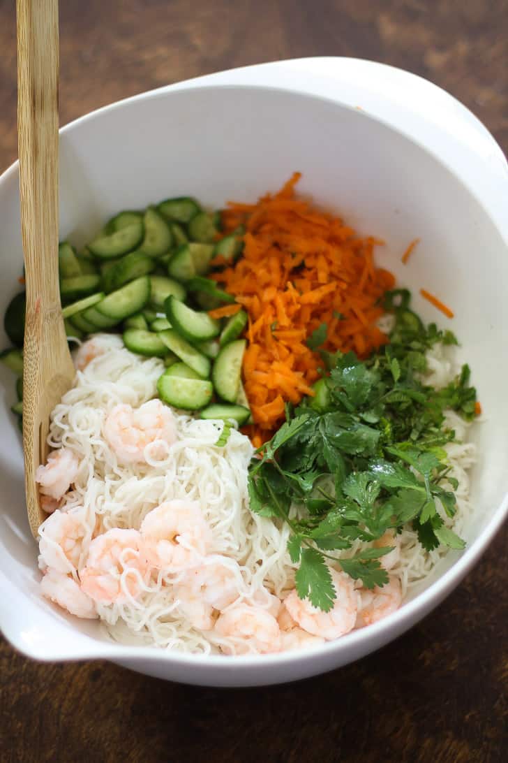 shrimp, noodles, vegetables and cilantro in a white bowl