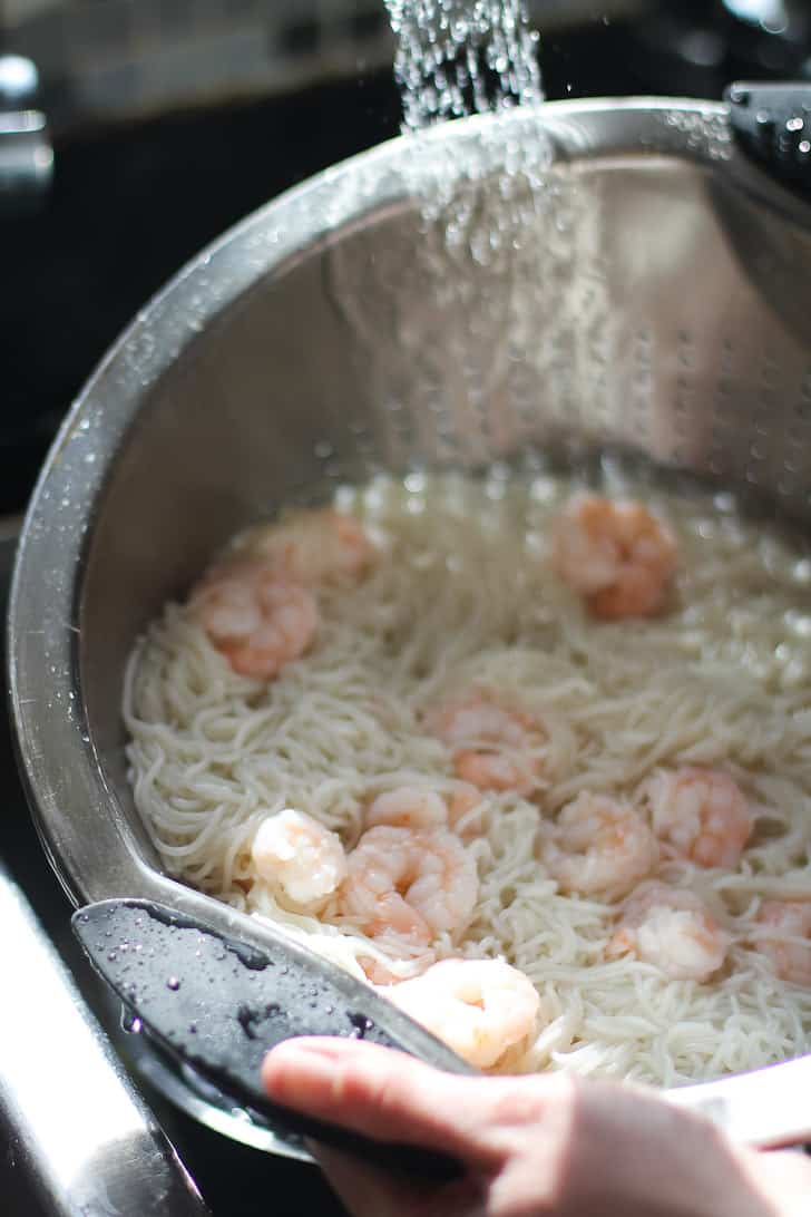 rinsing shrimp and noodles in a colander