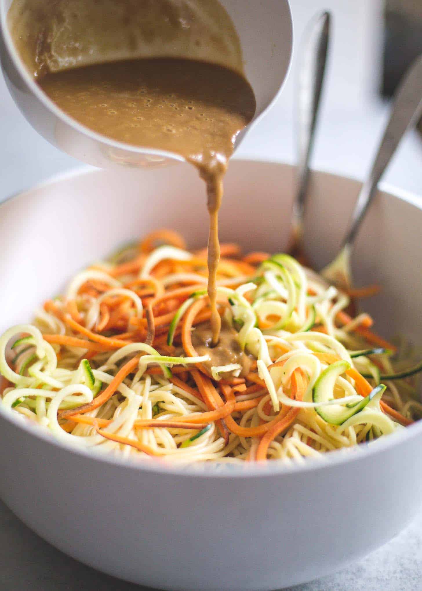 adding peanut sauce to noodles in a white bowl
